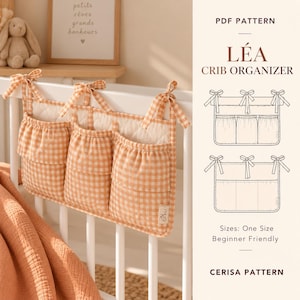 May include: A PDF pattern for a crib organizer titled LÉA CRIB ORGANIZER by CERISA PATTERN. The image shows a three-pocket hanging organizer made of orange and white gingham fabric with tie-top straps, alongside technical line drawings.