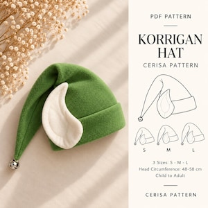 Puede incluir: Un gorro verde con un aplique blanco en forma de oreja y un pequeño cascabel plateado en la punta. El texto dice PDF PATTERN KORRIGAN HAT CERISA PATTERN. Incluye un dibujo lineal del gorro en tallas S, M y L para contornos de 48-58 cm.