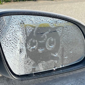 以下が含まれることがあります： 車のリアビューミラーに、大きく見開いた目と驚いた表情の漫画のキャラクターが描かれた白黒のステッカーが貼られています。ミラーは水滴で覆われています。ステッカーは、オーストラリア全土で無料配送を提供し、世界中に発送しているオーストラリアの小さな企業、Cheeky Stickeesのものです。