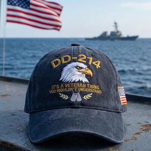 May include: A navy blue baseball cap with the text "DD-214" and an eagle design. The cap also features the phrase "It's a Veteran Thing You Wouldn't Understand" and a small American flag patch on the side. An American flag waves in the background.