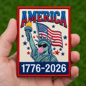 Puede incluir: Un parche bordado rectangular con borde rojo sobre fondo crema. Presenta la palabra AMERICA en azul y rojo, la Estatua de la Libertad con gafas de sol y una burbuja de chicle rosa, una bandera de EE. UU., estrellas y el texto 1776-2026 en blanco.