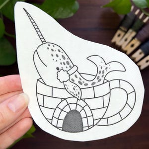 Könnte beinhalten: Schwarz-Weiß-Illustration eines Narwals in einem Iglu. Der Narwal hat ein langes Horn und ist mit Punkten verziert. Das Iglu hat einen abgerundeten Eingang. Das Bild befindet sich auf einem weißen, unregelmäßig geformten Aufkleber.