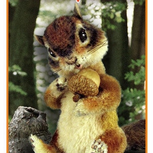 May include: A 5" plush chipmunk toy holding an acorn. The chipmunk is brown and white with a fluffy tail. The toy is sitting on a tree branch in a forest setting. The text "Mary Jardin Wimberley's 5" Chipmunk" is at the top of the image. The text "My Secret Garden" is at the bottom of the image.
