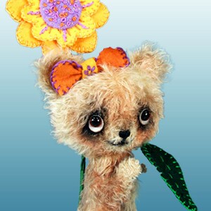 May include: A small, furry, brown teddy bear wearing a yellow flower on its head and an orange bow. The bear is holding a green leaf in its paw.