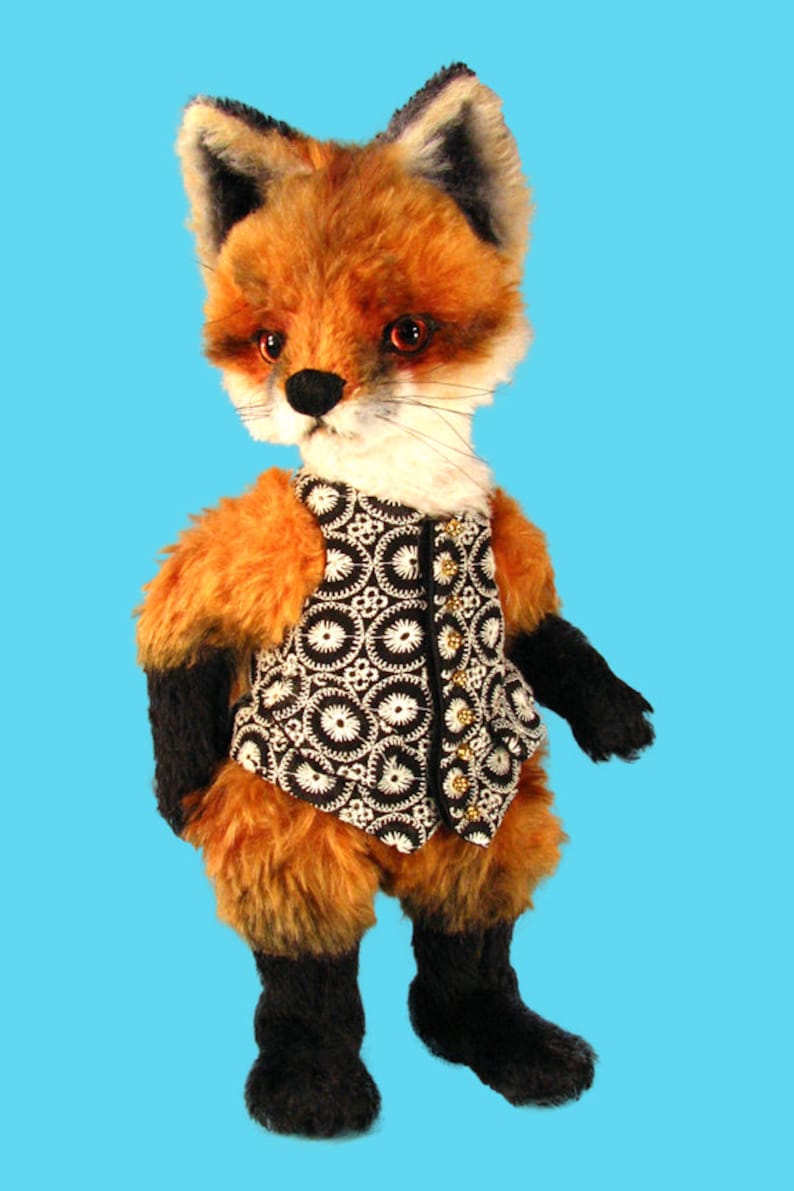 May include: A plush fox toy wearing a black and white patterned vest with gold buttons. The fox has orange fur, black eyes, and a black nose.