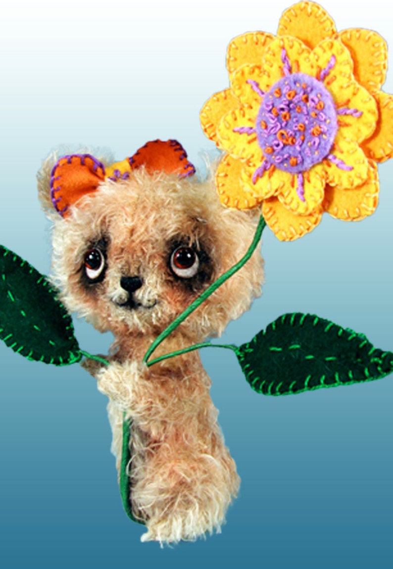 May include: A plush teddy bear with brown fur and big eyes holds a yellow felt flower with a purple centre. The flower is attached to a green felt stem with two green leaves.