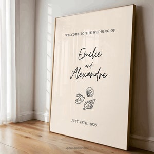May include: A beige wedding sign with black text that reads "Welcome to the wedding of Emilie and Alexandre" with a date of July 29th, 2025. The sign also features three black and white illustrations of seashells.