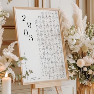 以下が含まれることがあります： 明るい木製フレームの額入りプリント。手描きの顔が並び、大きな黒いフォントで2903の数字が描かれています。Julie & Williamの名前が下部に印刷されています。木製のイーゼルにプリントが飾られています。