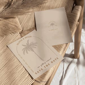 Könnte beinhalten: Zwei beige Hochzeitskarten mit Palmenillustrationen. Eine Karte zeigt den Text "Olivia & Peter" und "Save the Date". Die andere Karte hat den Text "Olivia & Peter" und das Datum "14.06.2025".