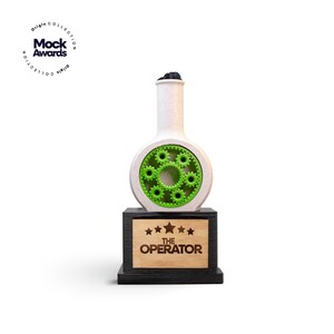 May include: A white and green trophy with a gear design inside a circular opening. The trophy sits on a black base with a wooden plaque that reads "THE OPERATOR" and has five stars. The trophy has a unique, modern design.