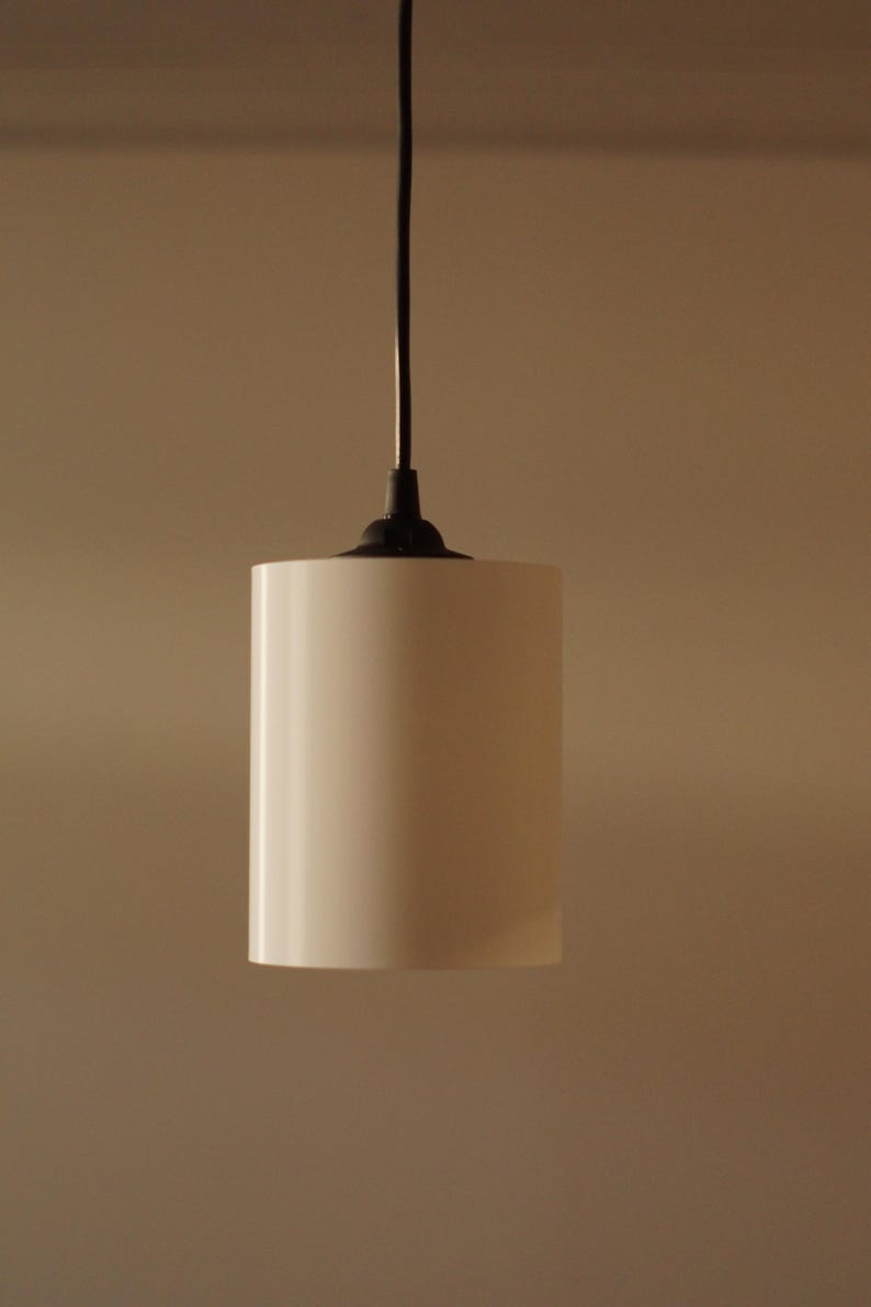 Pu&ograve; includere: Una lampada a sospensione cilindrica con finitura bianca opaca. &Egrave; appesa a un cavo nero e a un supporto a soffitto nero. Il design della lampada &egrave; minimalista e moderno, adatta a vari stili di interni.