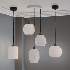 Pu&ograve; includere: Quattro lampade a sospensione bianche con cavi neri e supporti a soffitto. I paralumi hanno forme diverse: un cilindro, una sfera, un design sfaccettato e un motivo a spirale. Le luci sono sospese da un soffitto bianco.