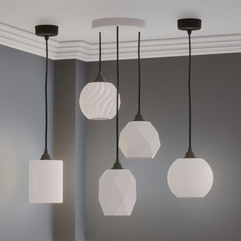 Pu&ograve; includere: Quattro lampade a sospensione bianche con cavi neri e supporti a soffitto. I paralumi hanno forme diverse: un cilindro, una sfera, un design sfaccettato e un motivo a spirale. Le luci sono sospese da un soffitto bianco.