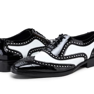 Può includere: Scarpe Oxford in pelle nera e bianca con design a punta alare e chiusura con lacci.