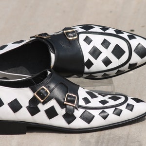 May include: A pair of black and white leather dress shoes with a diamond pattern. The shoes have double buckles and a pointed toe.