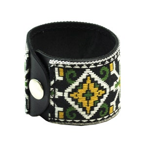 May include: Black leather cuff bracelet with a green, white, and gold geometric pattern.