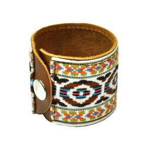 May include: A brown leather cuff bracelet with a colorful geometric pattern woven into the band. The bracelet has a snap closure.