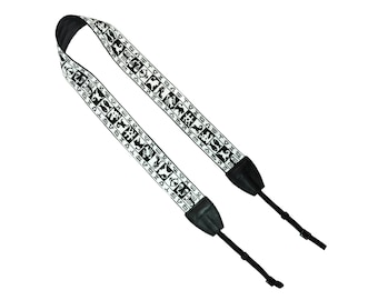 May include: Black and white camera strap with a repeating pattern of small black symbols on a white background. The strap has black leather ends with adjustable straps.