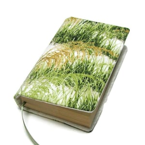 May include: A hardback book with a fabric cover displaying a green and gold grass design. It includes a light green ribbon bookmark. The book's edges are light brown.