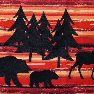 May include: Black felt cutouts of a bear, a moose, and a group of pine trees on a red and brown striped background.