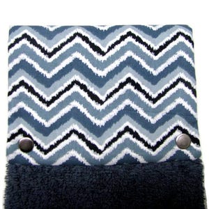 May include: A hanging kitchen towel featuring a blue, white, and black chevron pattern. The top section has a zigzag design, while the bottom is a dark blue, plush fabric. Two metal press studs secure the towel.