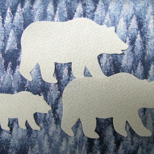 May include: Three white paper bear cutouts on a blue and silver background. The bears are layered on top of each other, with the largest bear at the bottom and the smallest bear at the top.