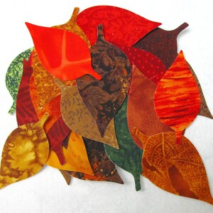Peut inclure: Une collection de feuilles en tissu dans différentes nuances de rouge, orange, marron et vert. Les feuilles sont découpées dans du tissu et présentent une variété de motifs et de textures.