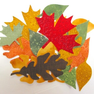 May include: A collection of felt leaves in various colours and patterns, including green, red, orange, and yellow. The leaves are arranged in a cluster, creating an autumn-themed design.