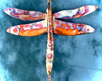 May include: A copper dragonfly wind chime with iridescent wings and a blue glass bead at the bottom.