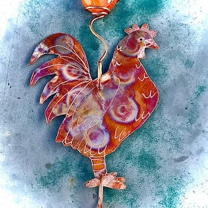 May include: A copper rooster sculpture with a swirling pattern and an orange glass orb on top. The rooster is standing on a metal rod.