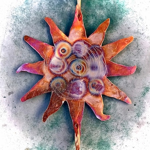 May include: A copper sun with a textured surface and a swirling pattern of purple, blue, and white. The sun is attached to a metal rod.