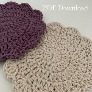 May include: Two crocheted coasters, one in a light beige color and one in a deep purple color. The coasters are round with a scalloped edge. The text "Pattern Only! PDF Download" is visible at the top of the image.