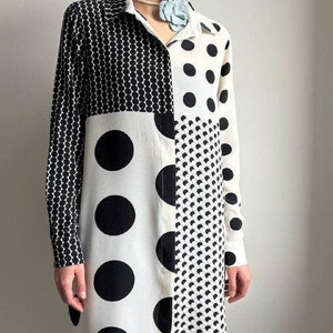 May include: A long-sleeved white shirt with a black and white polka dot pattern. The shirt is made of a lightweight fabric and has a relaxed fit.