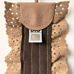 May include: A tan leather accessory with a perforated edge and a brown striped center. The accessory has a small leather flap with the brand name and measurements of 75 cm / 30 inch. A brand tag is visible.