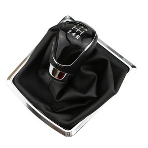 May include: A black leather gear shift boot with a silver trim and a black gear shift knob with silver lettering that reads "1 3 5, 2 4 R".