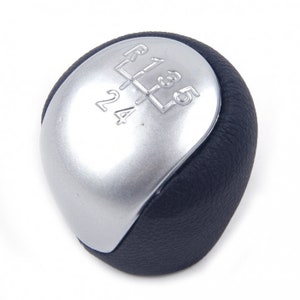 Può includere: Un pomello del cambio marcia in argento e nero con uno schema a 5 marce. Il pomello è rivestito in pelle e ha una parte superiore argentata con i numeri 1, 2, 3, 4, 5 e R.