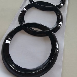May include: Four black interlocking rings, resembling the Audi logo, are arranged vertically on a white surface.