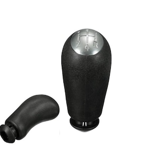 May include: A black gear shift knob with a silver top featuring the numbers 1, 2, 4, 5, and R. The knob is accompanied by a smaller black gear shift knob.