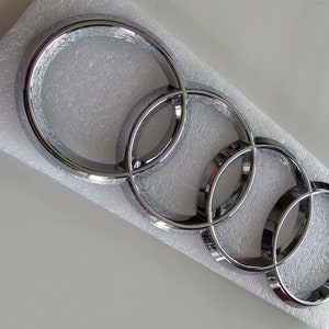 Puede incluir: Un emblema de coche plateado con cuatro anillos entrelazados.