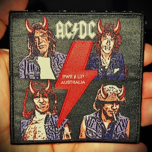 Może przedstawiać: Czarno-biała łatka z czerwonym błyskawicą. Łatka przedstawia zespół AC/DC i napis "PWR UP AUSTRALIA".