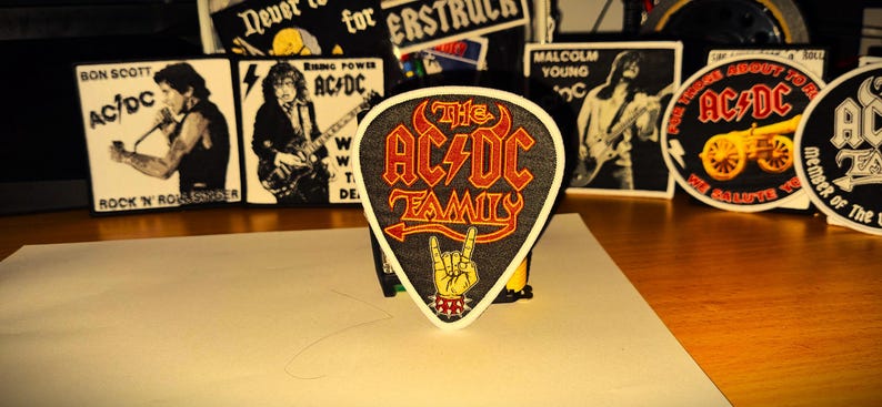 Peut inclure: Un &eacute;cusson brod&eacute; noir et rouge en forme de m&eacute;diator de guitare avec le texte "The AC/DC Family" et un &eacute;clair.