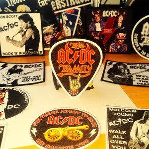 Peut inclure: Une collection de patchs et d'autocollants de groupe AC/DC color&eacute;s. Les patchs pr&eacute;sentent divers membres du groupe, des pochettes d'album et des paroles. Les autocollants sont principalement en noir et blanc avec quelques-uns en couleur. Les patchs et les autocollants sont tous sur une surface en bois.