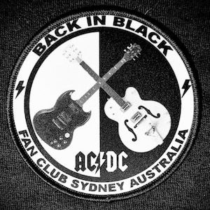 May include: Black and white circular patch with the text "Back in Black" and "AC/DC" in a bold font. The patch also features the text "Fan Club Sydney Australia" and two crossed electric guitars.