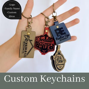 May include: Four custom leather keychains with different designs and text. The keychains are brown, red, blue, and black. The text on the keychains includes "Seattle Butcher's Wife", "Realtors Edge Branding", "The Bess Insurance Agency", and "Batoholer & Co."