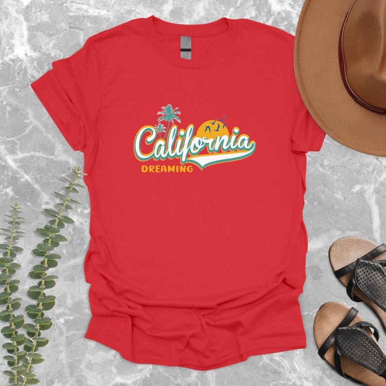 May include: Red t-shirt with a retro-style graphic that says "California Dreaming" with palm trees and a sunset.