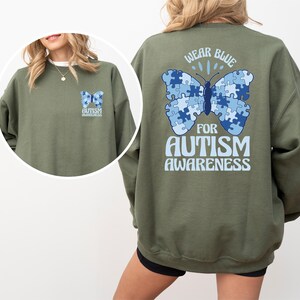 Pu&ograve; includere: Felpa verde con una farfalla blu fatta di pezzi di puzzle sul retro. La farfalla ha il testo "Wear Blue for Autism Awareness".