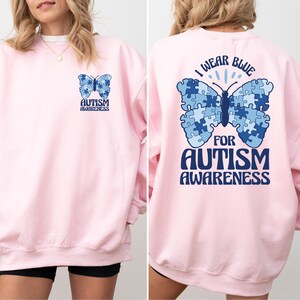 Pu&ograve; includere: Felpa rosa con una farfalla blu fatta di pezzi di puzzle sul retro. La farfalla ha il testo "Indossare il blu per la consapevolezza dell'autismo". La parte anteriore della felpa ha una farfalla blu pi&ugrave; piccola con il testo "Consapevolezza dell'autismo".