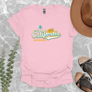May include: Pink t-shirt with a graphic design of palm trees, a sunset, and the text "California Dreaming".