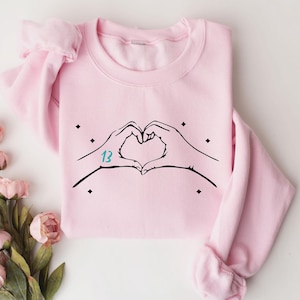 May include: Pink sweatshirt with a black hand heart design and the number "13" in teal blue.