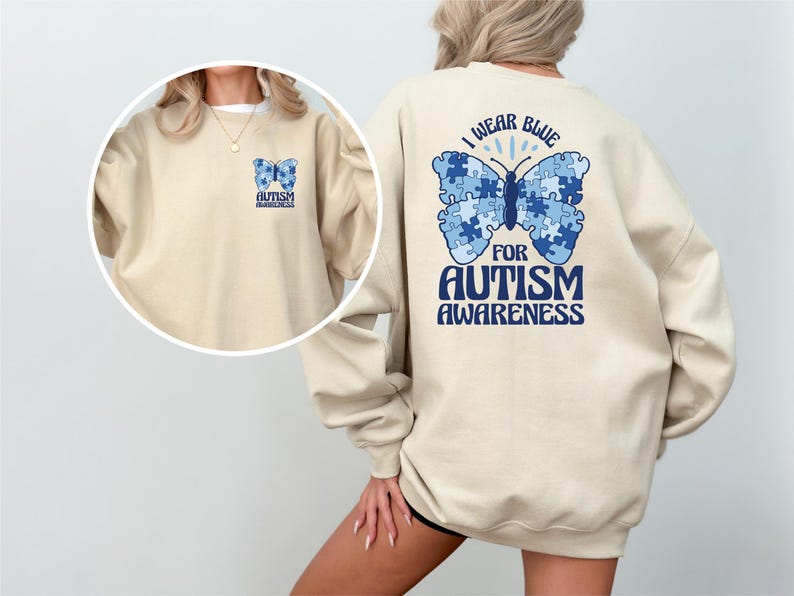 Pu&ograve; includere: Una felpa beige con una farfalla blu fatta di pezzi di puzzle sul retro. La farfalla ha il testo "Indossare il blu per la consapevolezza dell'autismo". La parte anteriore della felpa ha una farfalla blu pi&ugrave; piccola con il testo "Consapevolezza dell'autismo".